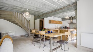 Un comedor amplio con una mesa y sillas de madera, una escalera y una zona de cocina con armarios de madera y electrodomésticos modernos.