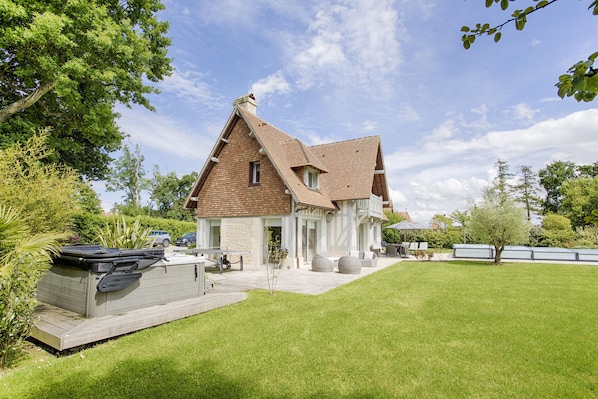 A two-story house with a sloped roof, a covered patio, and a well-maintained lawn.