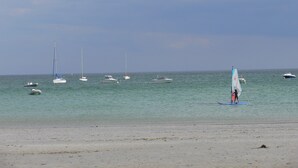 Una playa con varios veleros y una persona practicando surf.