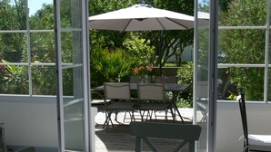 Un patio con paredes de vidrio que incluye una mesa y sillas, rodeado de abundante vegetación.