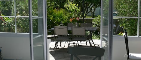 A glass-enclosed patio with a table and chairs, surrounded by lush greenery.