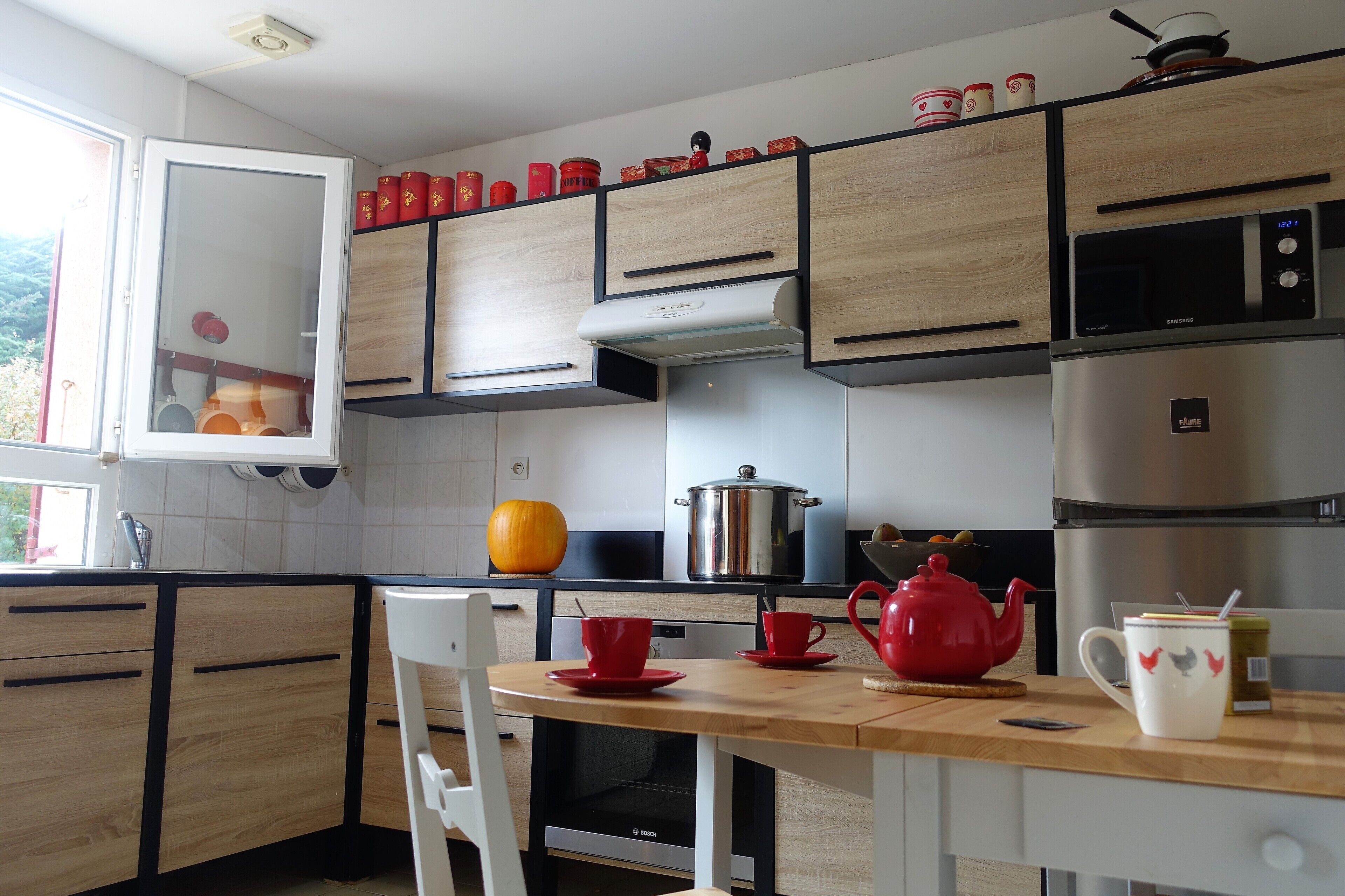 A modern kitchen with wooden cabinets, a stainless steel refrigerator, a Bosch dishwasher, and a red teapot on the counter.