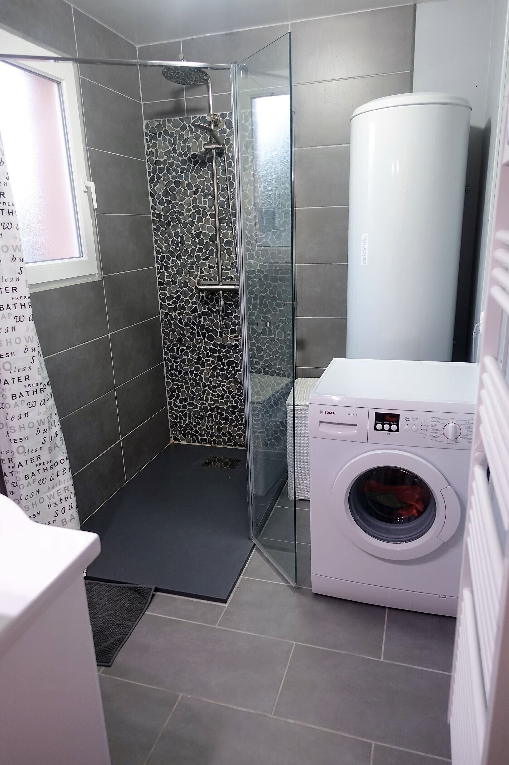 A modern bathroom with a shower, a Bosch washing machine, and a large water heater.