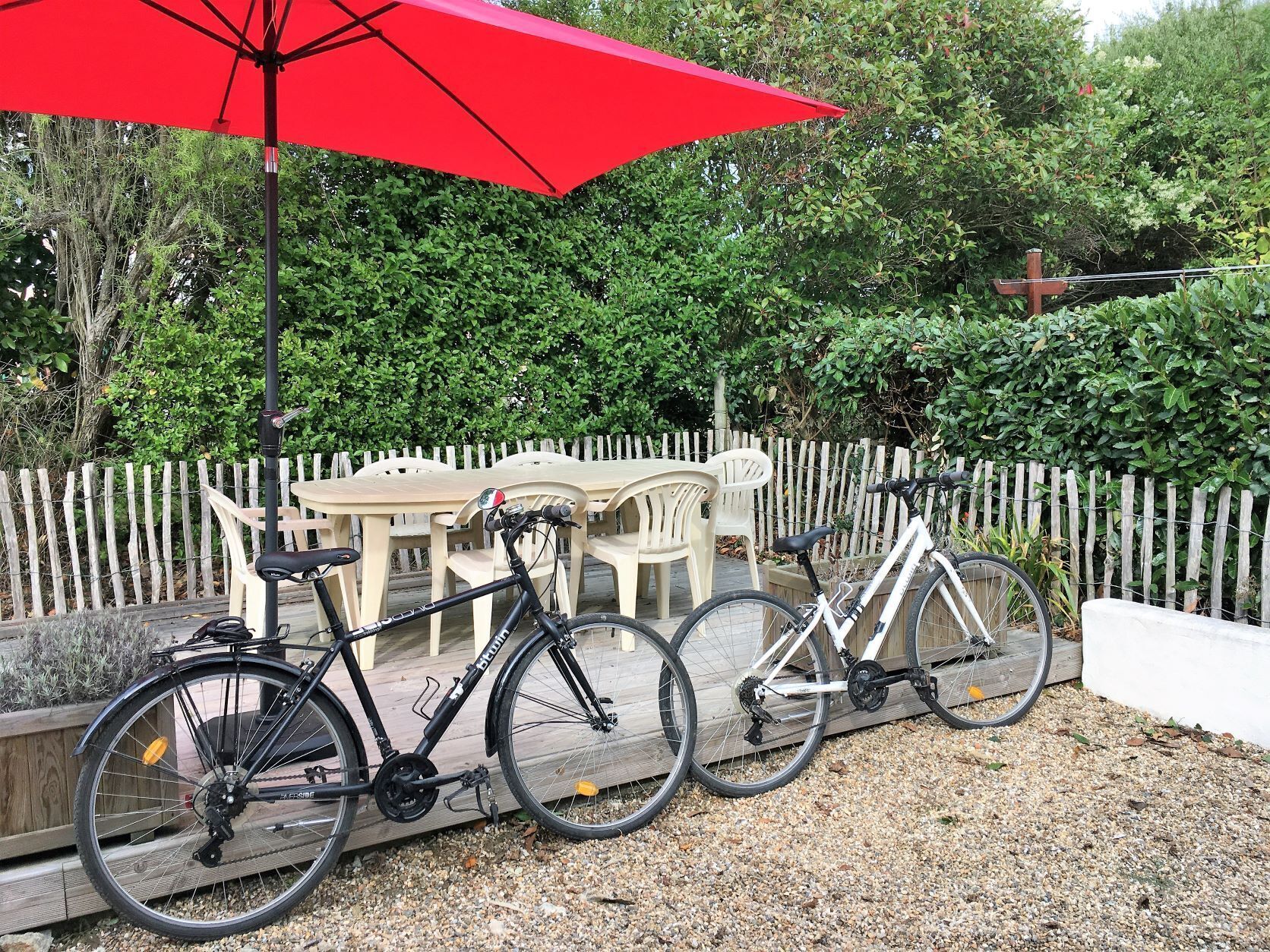 Een fiets geparkeerd naast een witte plastic tafel en stoelen, met een rode parasol erboven.