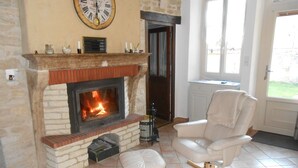 Ein Wohnzimmer mit Kamin, einem weißen Ledersessel, einem Holzschemel und einer Wanduhr.