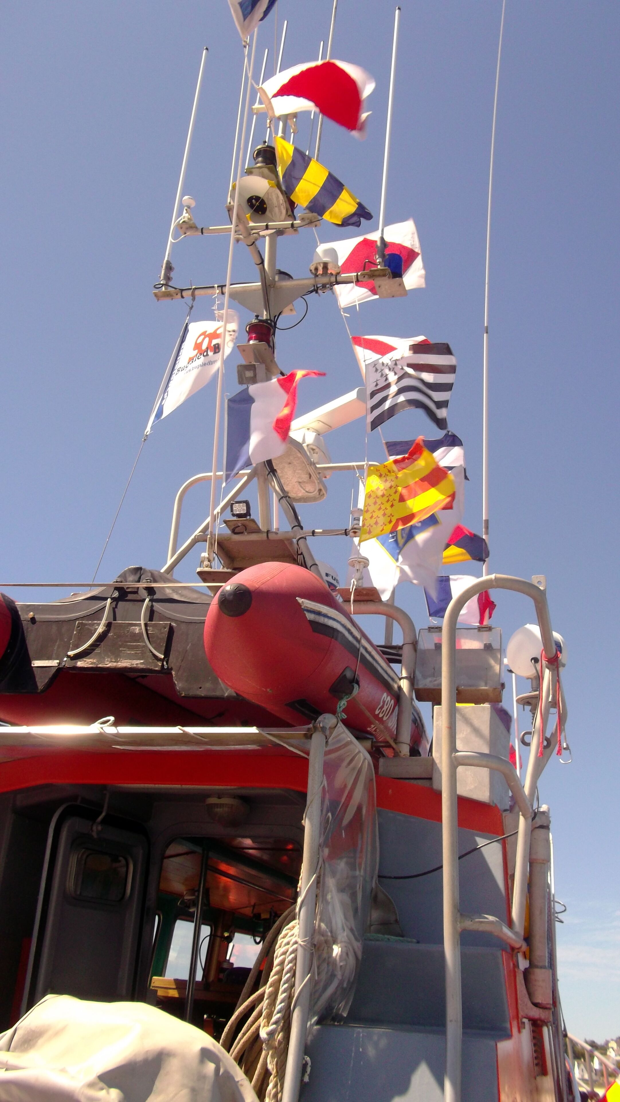 Cubierta de barco con varias banderas, un flotador salvavidas y un malacate.
