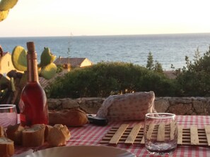 A table with bread, a bottle, and a glass, overlooking a body of water with houses in the background.