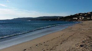A beach with clear blue water, sandy shore, and houses in the background. - villa marina , climatised,wi-fi, private garden and parking. (Sartène)