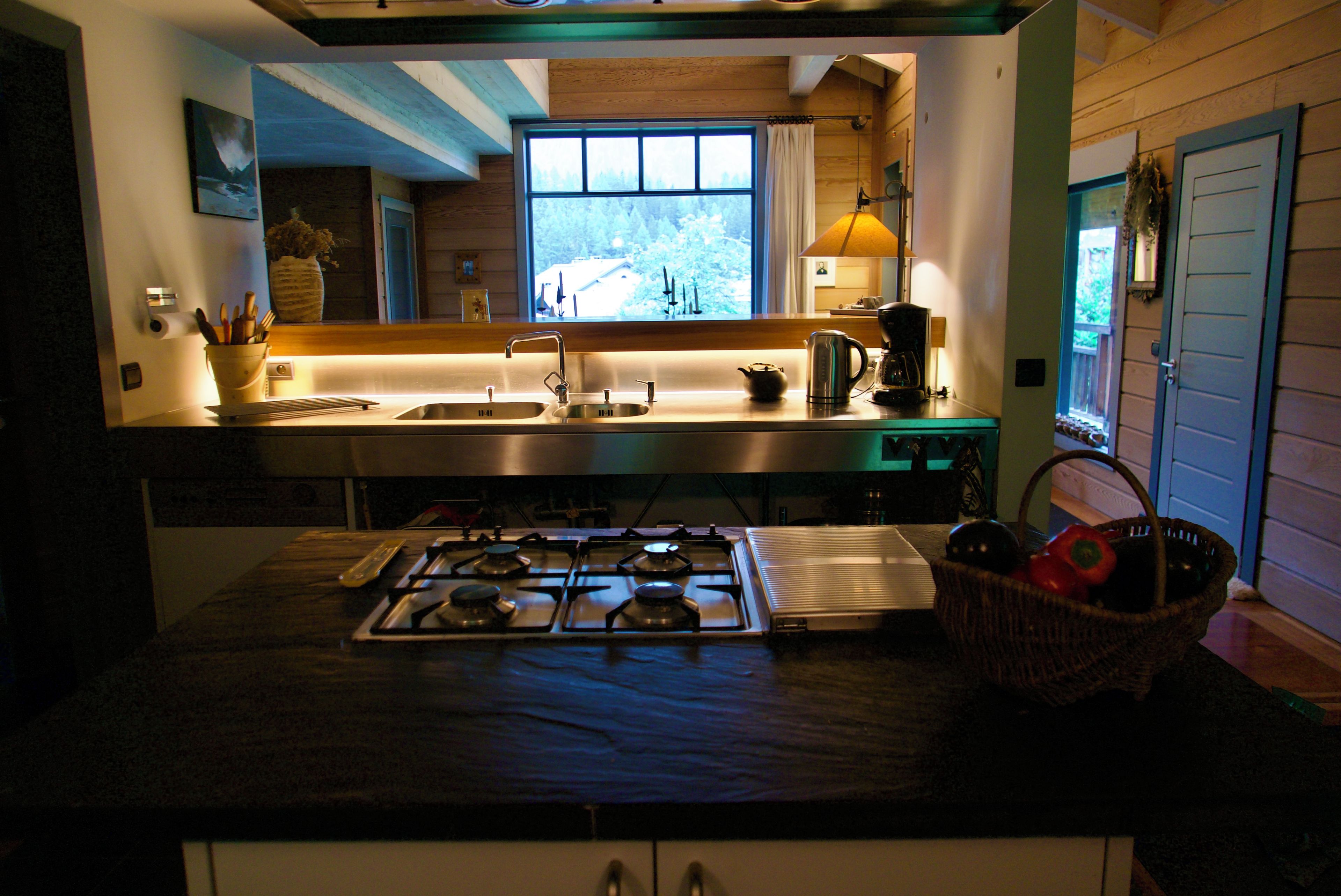A kitchen with a gas stove, sink, and a window with a view of trees.