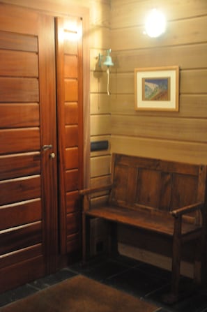 A wooden bench in a room with wooden panel walls, a framed picture, and a wall-mounted light fixture.