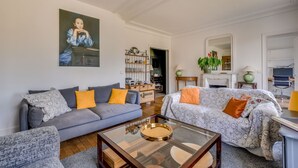 A living room with a sofa, armchair, coffee table, and a painting on the wall. - Cosy and spacious 145m² family apartment (Paris)