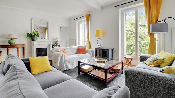 A living room with two sofas, a coffee table, a fireplace, and large windows with curtains. - Cosy and spacious 145m² family apartment (Paris)