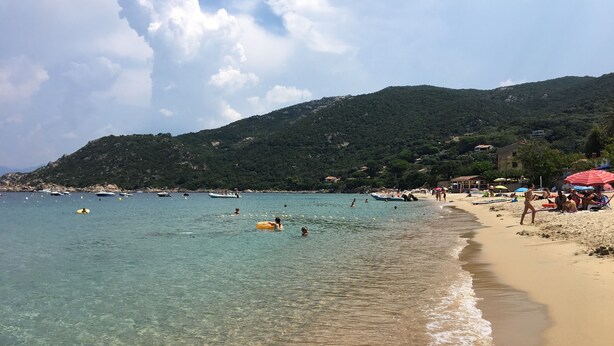 A beach with clear water, people swimming, and boats.