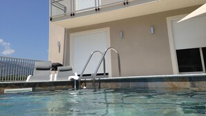 A swimming pool area with a metal ladder, lounge chairs, and a building with a balcony.