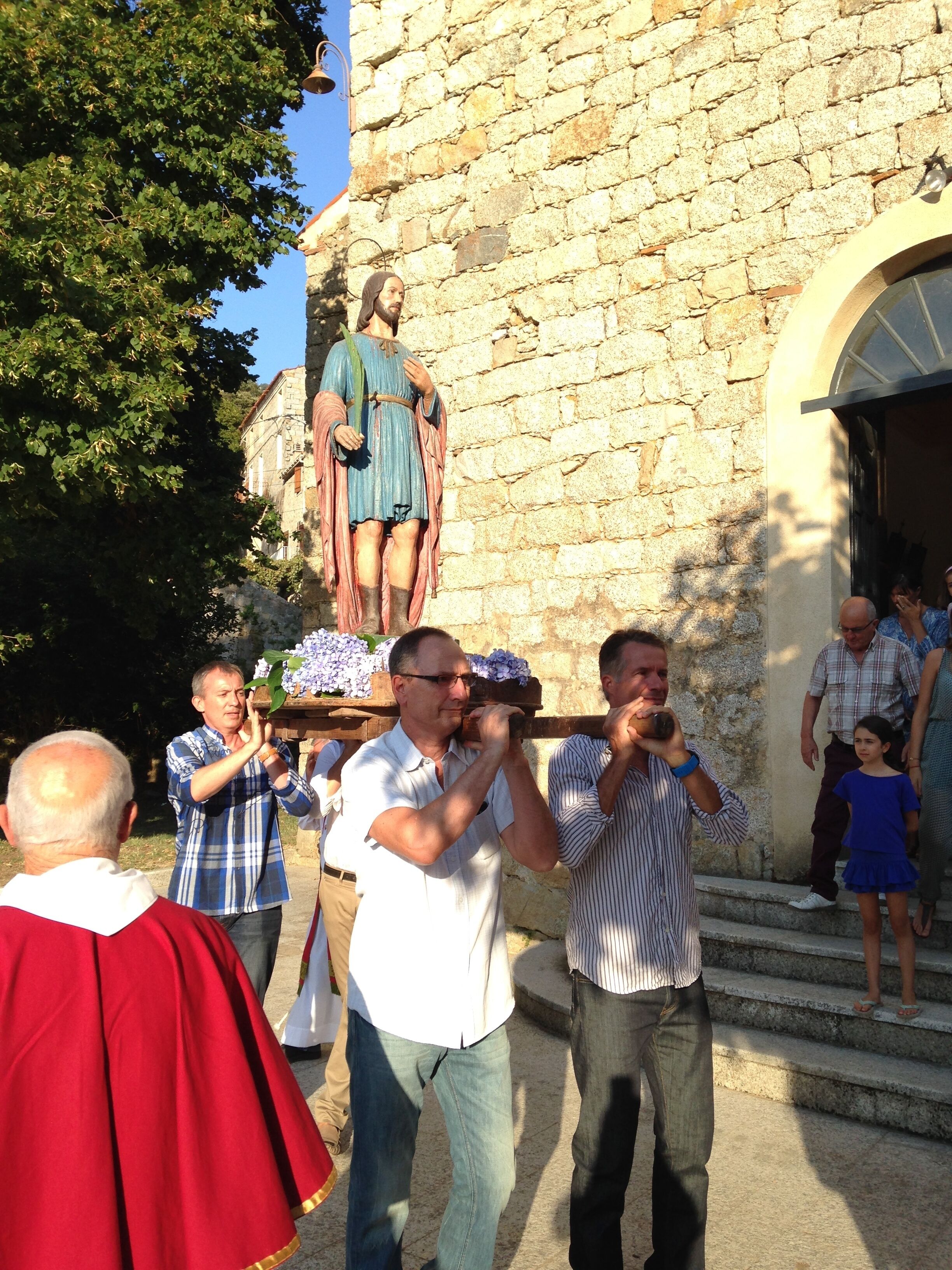 A stone building with a statue on a pedestal, steps leading up to the entrance, and people gathered around.