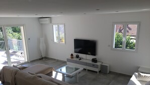 A modern living room with a sofa, a coffee table, a TV, and a sliding glass door leading to a balcony.