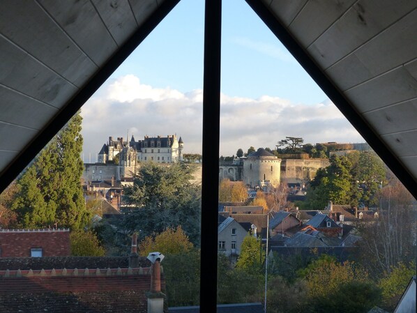 A view of a castle-like building with a moat and surrounding trees, viewed from a window with a triangular frame.
