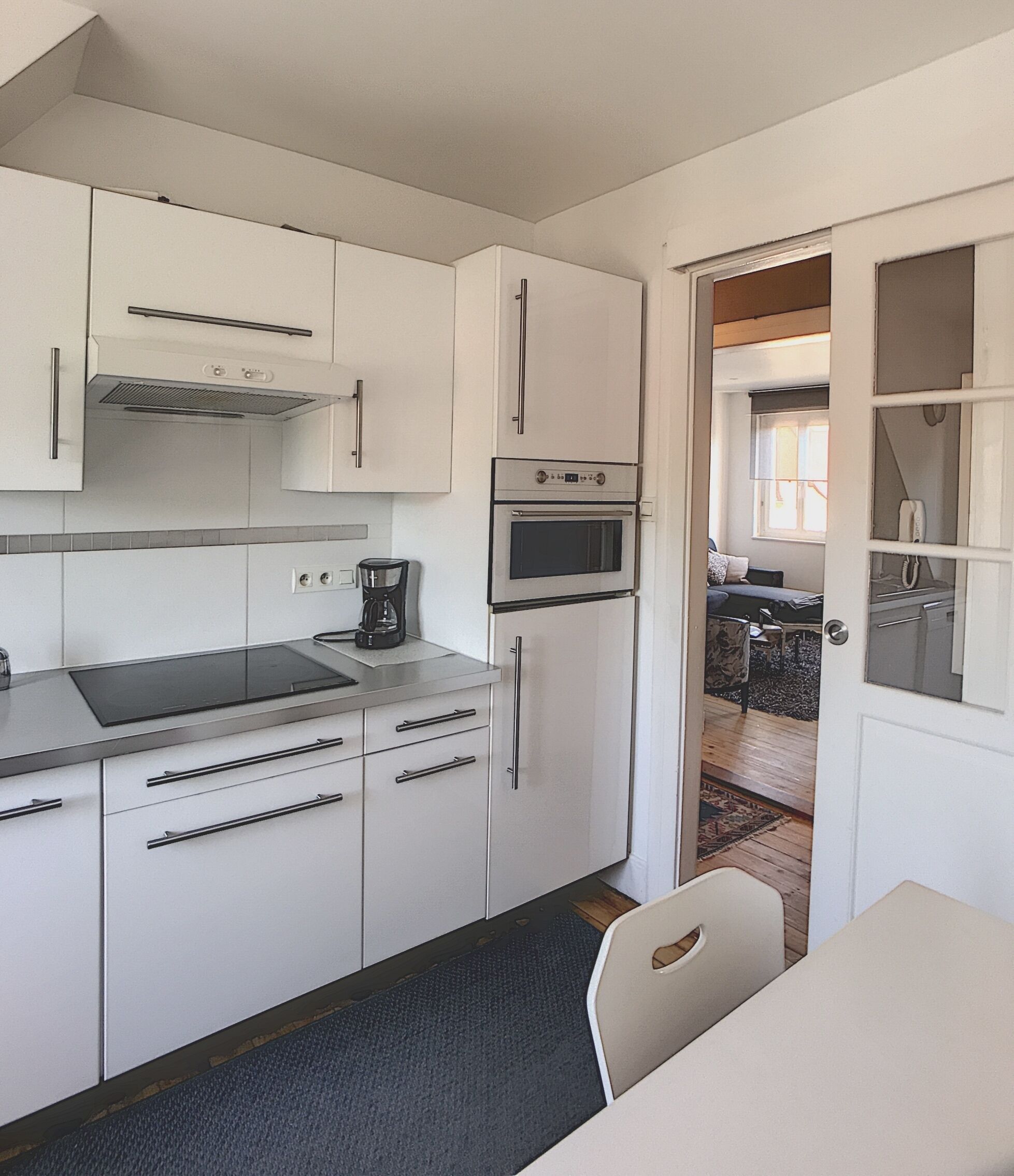 Una cocina compacta con armarios blancos, horno integrado y cafetera.