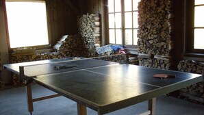 A ping pong table in a room with a large window, wooden walls, and stacks of firewood.
