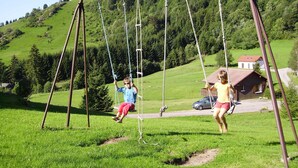 A swing set in a grassy area with a house in the background.