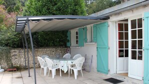 Une terrasse avec une table et des chaises, un espace abrité et un mur en pierre.