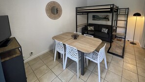 A compact room with a wooden dining table and white chairs, a bunk bed with a ladder, a small TV on a cabinet, and a floor lamp. - 100 metres from Santa Guilia beach, comfortable, garden furniture, barbecue (Porto-Vecchio)