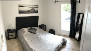 A bedroom with a bed, a nightstand, a bedside table, a window with curtains, and a wall-mounted picture. - 100 metres from Santa Guilia beach, comfortable, garden furniture, barbecue (Porto-Vecchio)