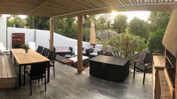 Relax on the patio surrounded by lush gardens and a pergola, featuring a sofa, chairs, and storage bench.