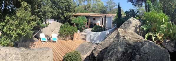 Una villa con terraza de madera, dos sillones blancos y un área de patio techada.