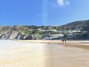 Una playa costera con cielos despejados, acantilados rocosos y edificios blancos con techos rojos.