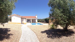 Ein Haus mit Pool, umgeben von Olivenbäumen und einem Kiesweg.