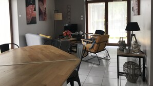 A dining area with a wooden table, chairs, and a television. There is a window with curtains and a view of the outdoors. - Bungalow, enclosed garden, direct beach access (La Turballe)