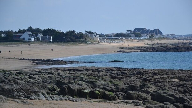 A beach with rocky terrain, a sandy shore, and buildings in the background. - Bungalow, enclosed garden, direct beach access (La Turballe)