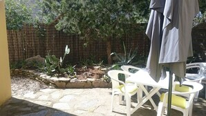 Un patio con piso de piedra, sillas de plástico blanco, una mesa y una valla de madera.