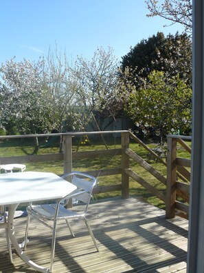 Relax on the deck surrounded by a serene garden with blooming trees and a swing set in the distance.