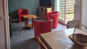 Una sala de estar con televisión, sillas rojas, una mesa de madera y un balcón con cerramiento de madera.