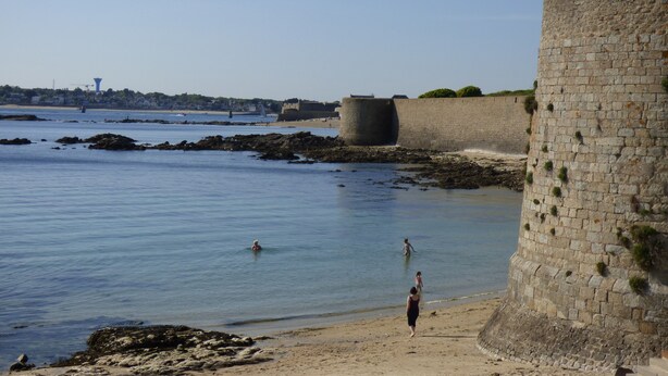 Un paisaje costero con un muro de piedra y una playa de arena.
