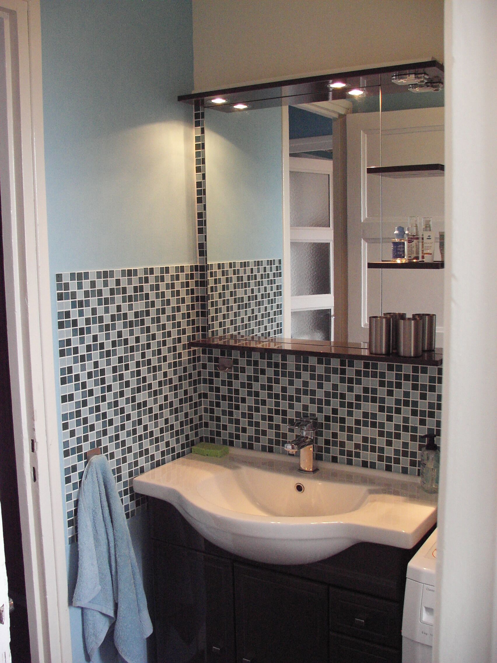 Un baño con salpicadero de azulejos, un lavabo, un espejo y un perchero para toallas.