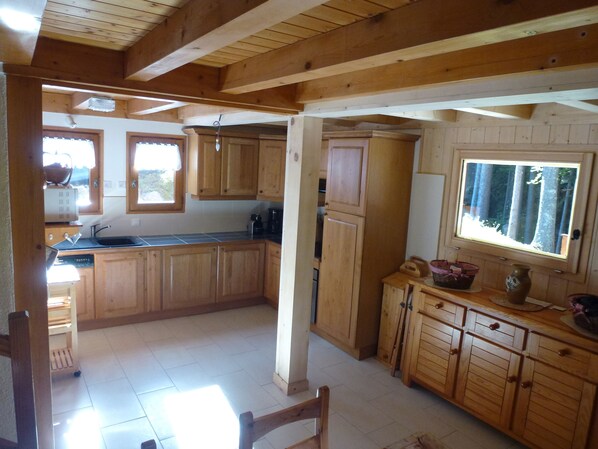 A wooden kitchen with a large window, wooden cabinets, and a tiled floor. - Independent chalet on 2 levels with parking and WIFI classified 3 stars (Arâches-La-Frasse)
