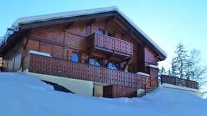 Een houten chalet met balkon, omgeven door sneeuw.