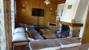 Een gezellige woonkamer met een hoekbank, een flatscreen televisie, een open haard en houten wanden.