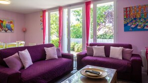 Une pièce avec des canapés violets, une table basse en verre et un tableau accroché au mur.