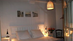 Un lit bien fait, avec des oreillers et des serviettes pliées, une table de chevet avec une lampe, une chaise et un mur orné de trois tableaux encadrés.