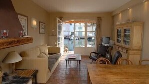A cozy living room with a sofa, coffee table, and a dining table. There is a television, a cabinet, and a window with curtains. - Fisherman's house in Port-Grimaud (Grimaud)
