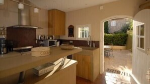 A compact kitchen with a built-in stove, a microwave, and a sink. There is a wooden cabinet above the counter and a window providing natural light. - Fisherman's house in Port-Grimaud (Grimaud)
