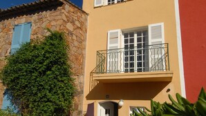 A two-story building with a balcony, stone walls, and a garden area with plants and a table. - Fisherman's house in Port-Grimaud (Grimaud)