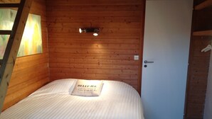 Une chambre avec un plafond en bois, un lit avec un oreiller, une porte et un luminaire.