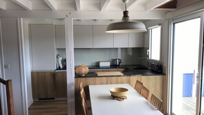 Une cuisine moderne avec un coin repas, dotée d’une grande fenêtre, d’un luminaire suspendu et de meubles de rangement en bois.