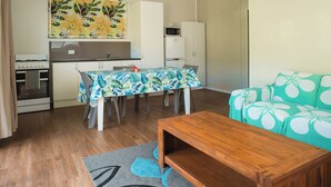 A compact living space with a dining table, a sofa, a wooden coffee table, a kitchen area with a microwave, and a refrigerator.