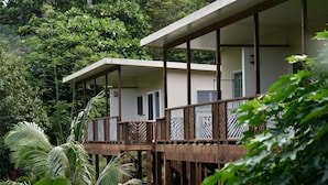 A modern bungalow with a balcony, surrounded by lush greenery.
